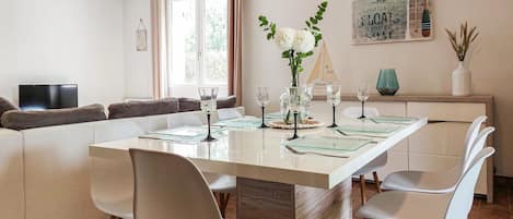A modern dining area with a white table, clear glassware, and a vase with white flowers.
