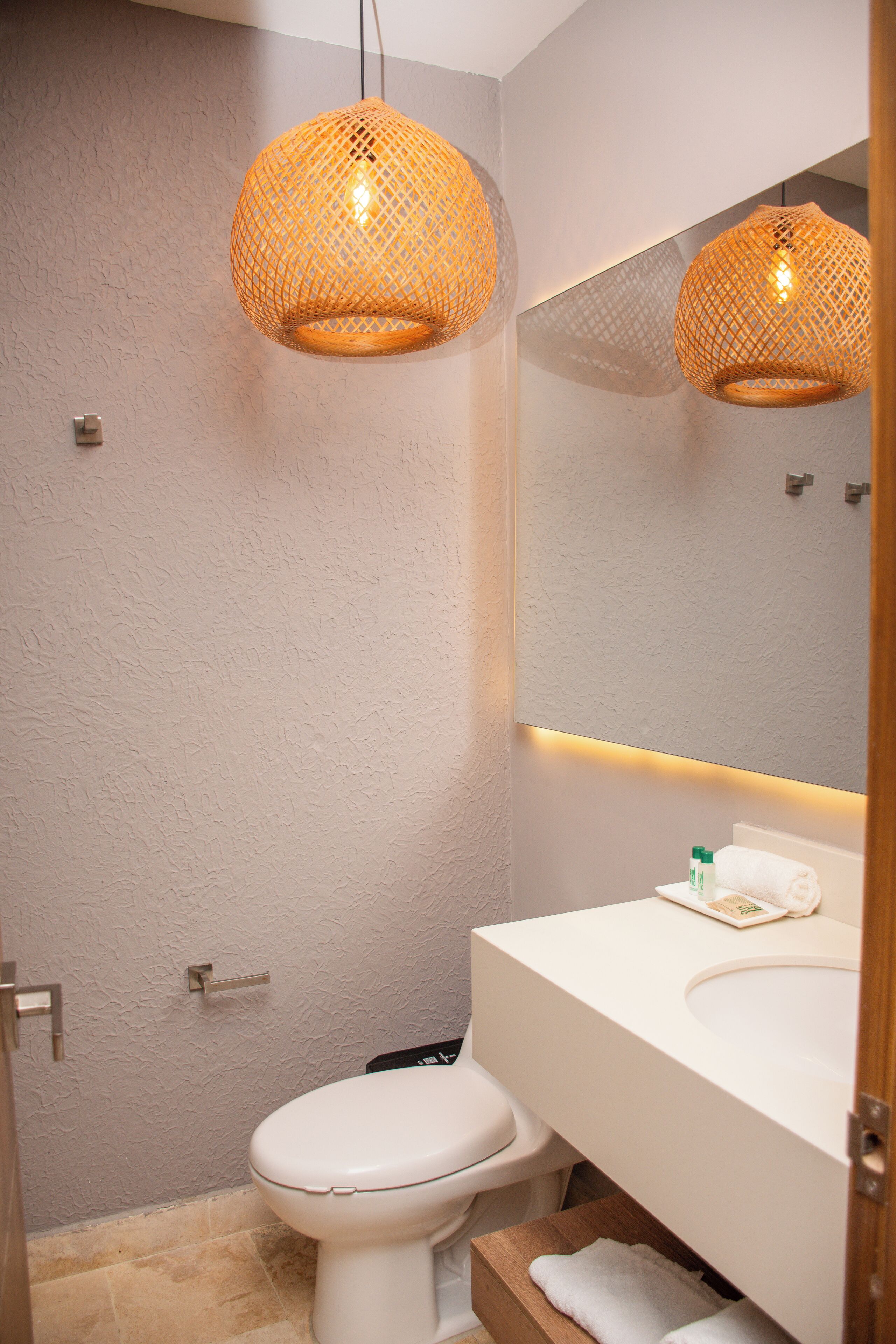 A bathroom with a toilet, a sink, and a mirror. There are two hanging lights above the mirror.