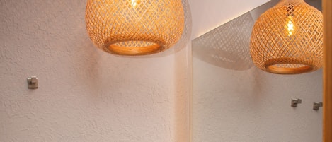 A bathroom with a toilet, a sink, and a mirror. There are two hanging lights above the mirror.