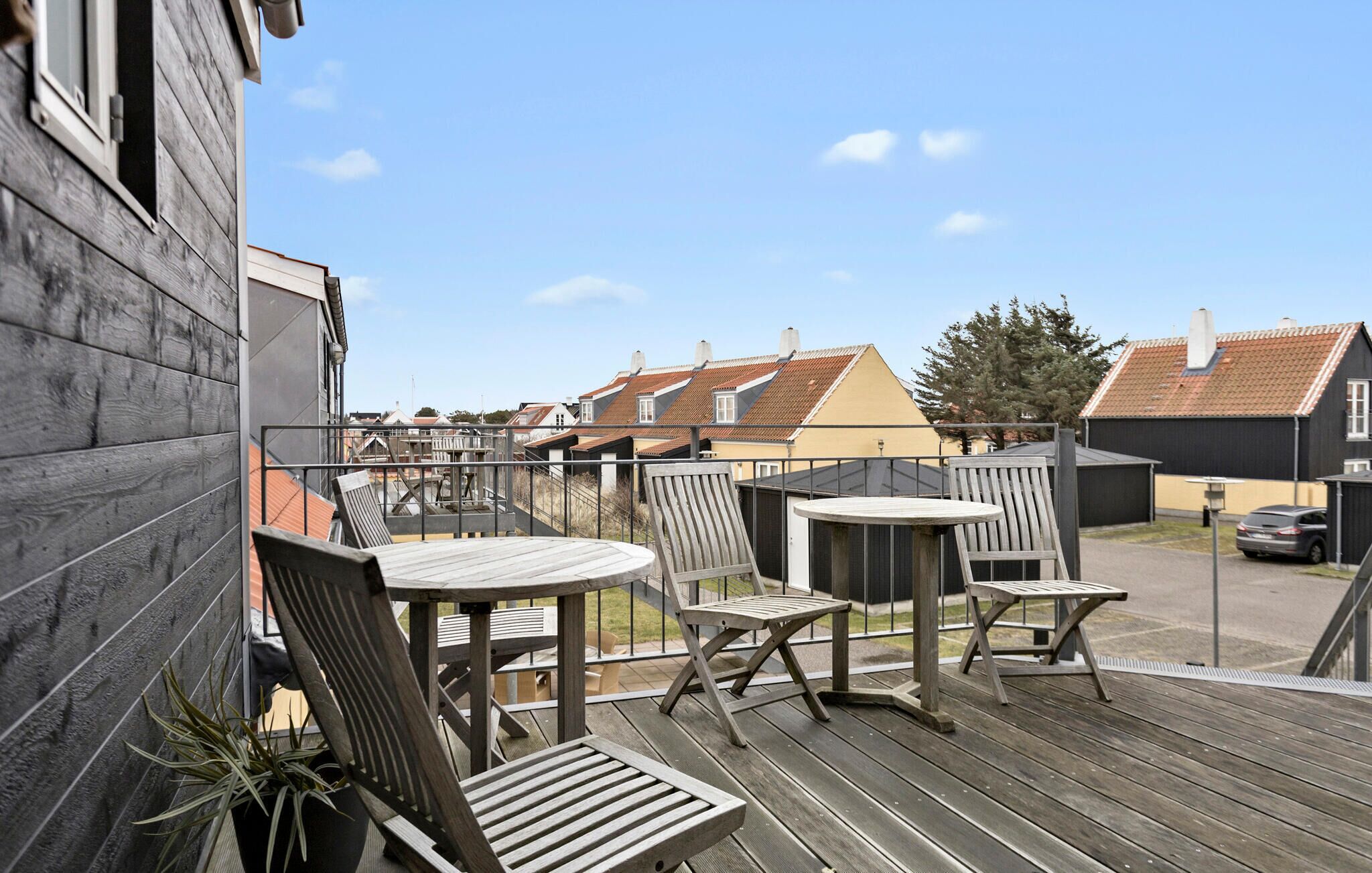 A wooden deck with outdoor furniture, a view of neighboring houses, and a clear sky.