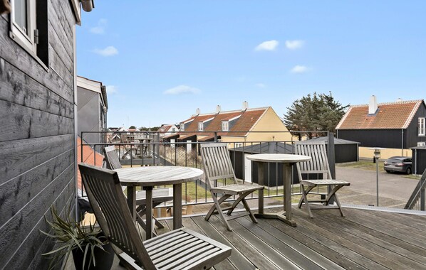 A wooden deck with outdoor furniture, a view of neighboring houses, and a clear sky.