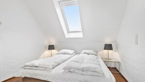 Un dormitorio con tragaluz, dos mesitas de noche con lámparas, cama con ropa de cama blanca y suelo de madera.