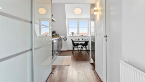 Un pasillo estrecho con una zona de cocina, una mesa de comedor con sillas y una ventana con vistas.