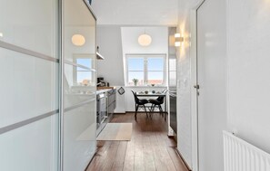 A narrow hallway with a kitchen area, a dining table with chairs, and a window with a view. - Beautiful apartment in Skagen with sauna (Skagen)