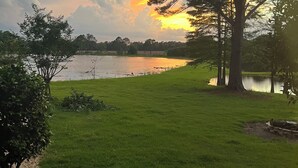 A grassy area with a lake, trees, and a sunset.