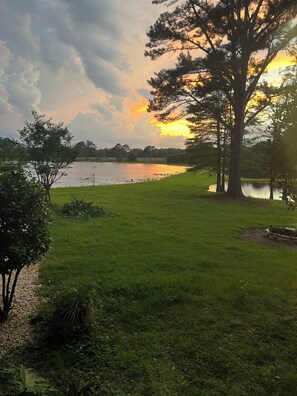 Un área con césped, un lago, árboles y un atardecer.