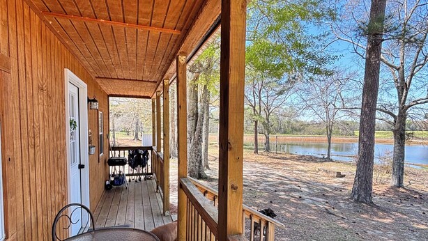 A wooden deck with a table and chairs, overlooking a lake and trees.