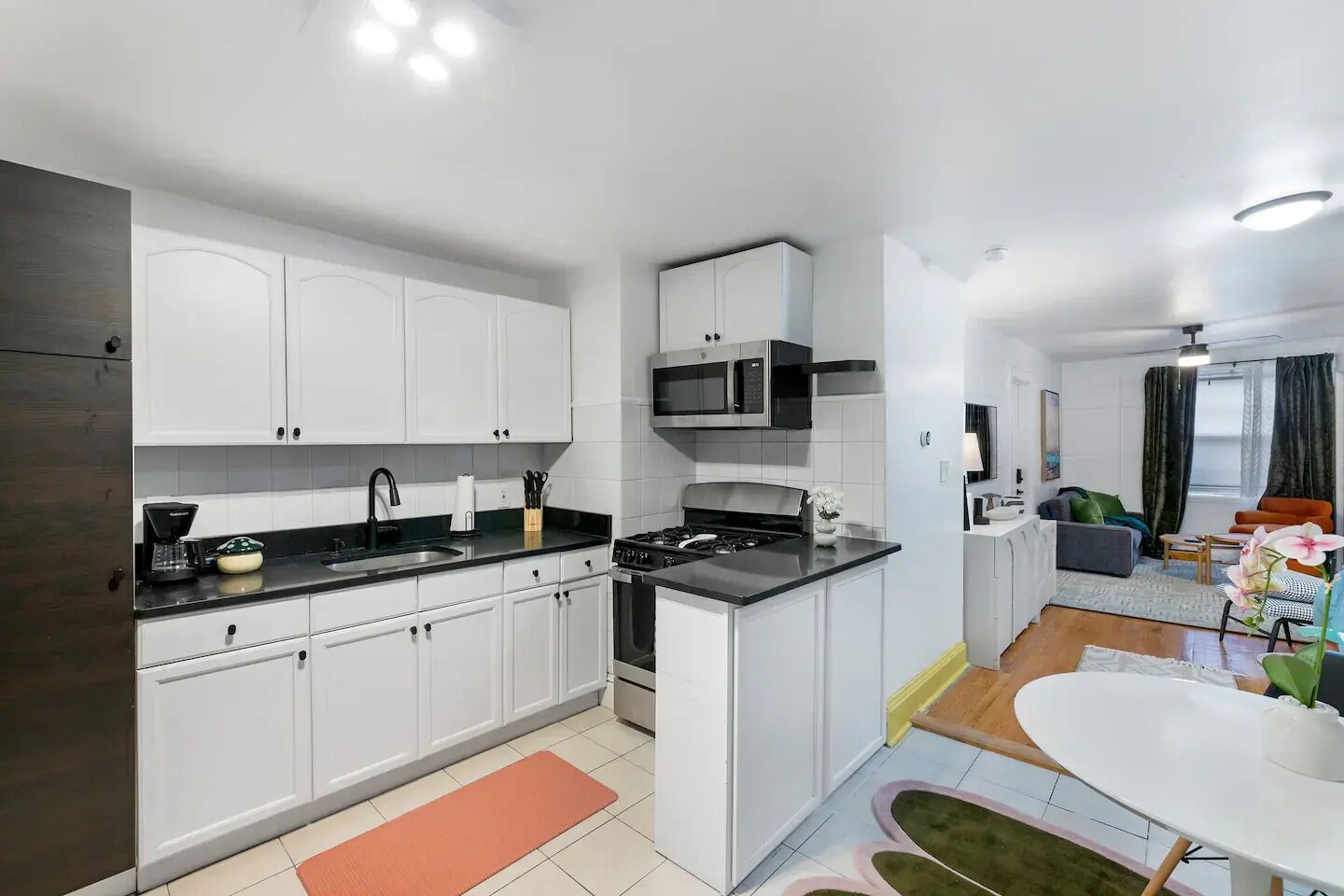 A modern kitchen with white cabinets, a black countertop, and a stove. There is a dining area with a white table and chairs.