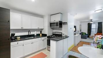 A modern kitchen with white cabinets, a black countertop, and a stove. There is a dining area with a white table and chairs.