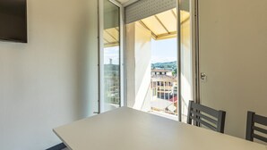 A balcony with a table and chairs, a sliding glass door, and a view of buildings and hills.
