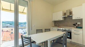 A modern kitchen with white cabinets, a stainless steel range hood, and a view of the city through a large window.
