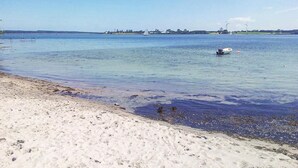 Una spiaggia con acque poco profonde e cristalline, una barca e turbine eoliche in lontananza.