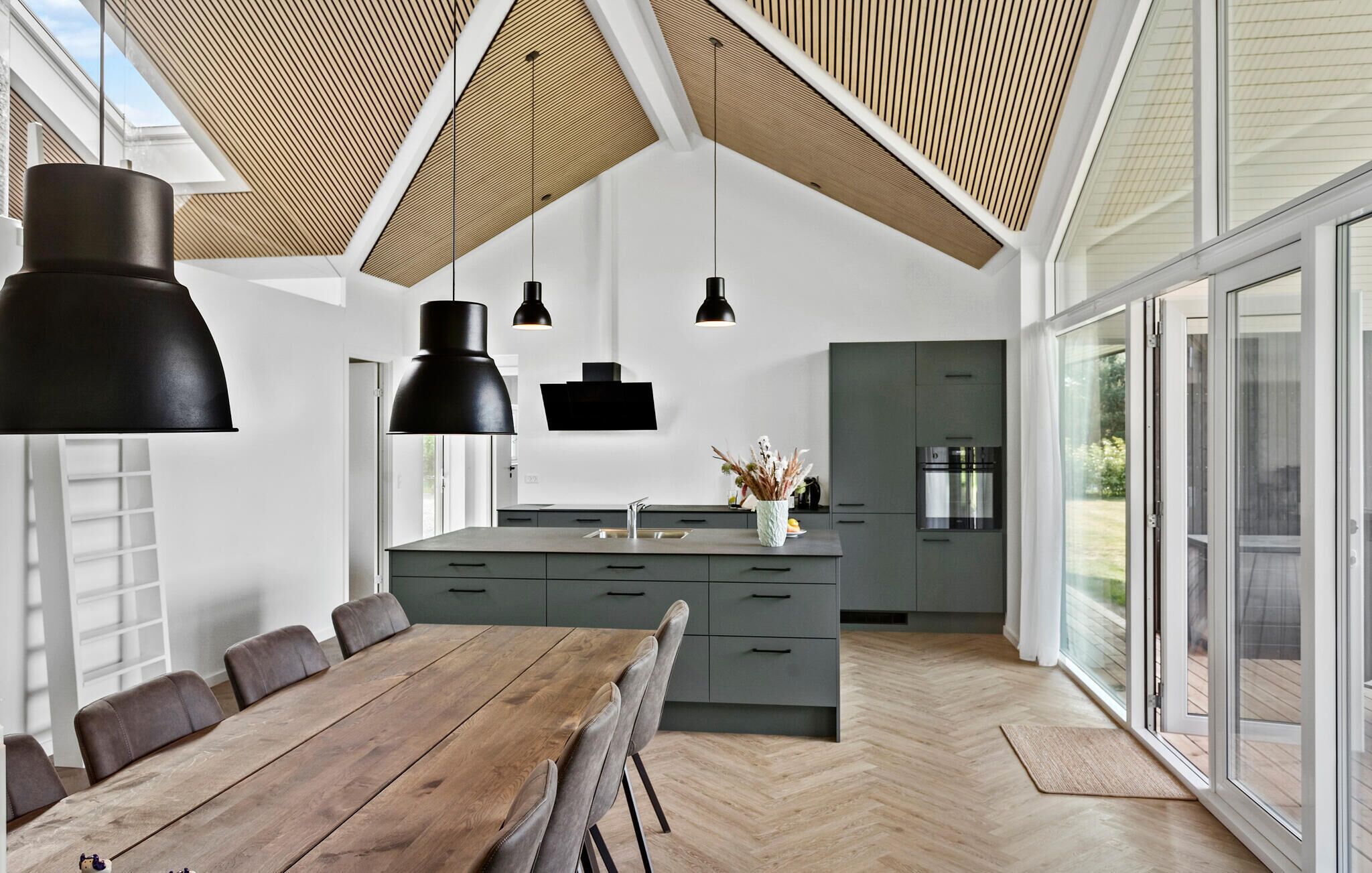 A modern kitchen with a central island, large windows, and a dining area with a wooden table and chairs.