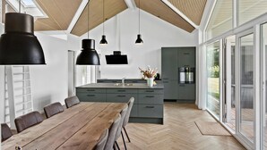A modern kitchen with a central island, large windows, and a dining area with a wooden table and chairs.