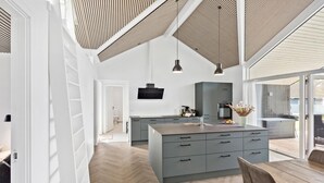 A modern kitchen with a large island, grey cabinetry, and pendant lighting.