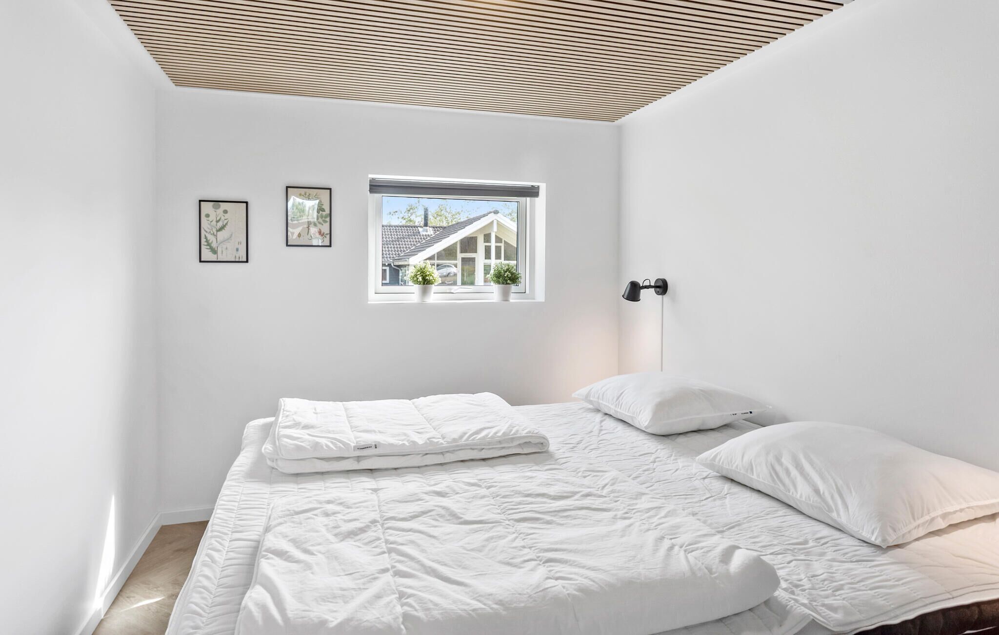 A bedroom with a bed, a window with a view of a house, and a ceiling with wooden slats.