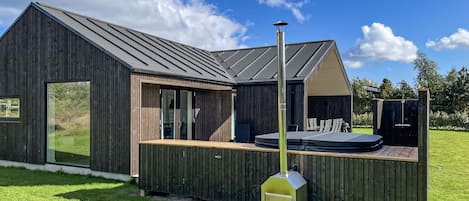 Una cocina moderna al aire libre con una parrilla integrada, una terraza de madera y un amplio ventanal con vistas a una zona verde.