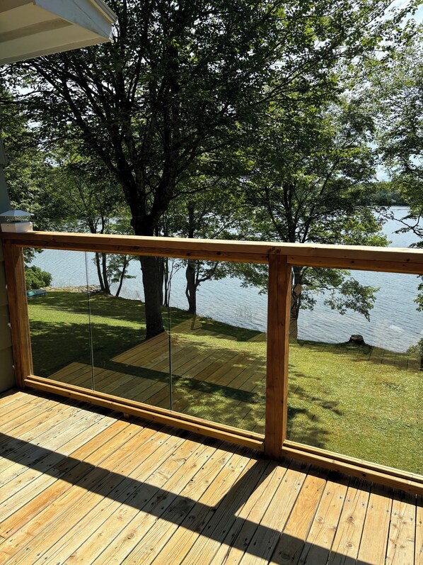 A wooden deck with a glass railing overlooking a lake and trees.