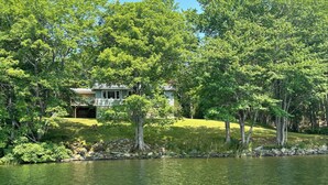 A house surrounded by lush green trees and a calm body of water.