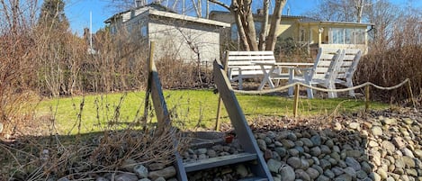 Une structure en pierre avec une échelle en bois menant à un espace agrémenté de bancs et de chaises blanches.