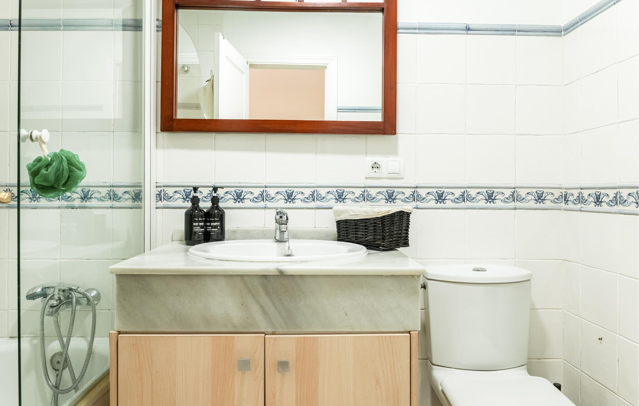 Un baño con lavamanos blanco, espejo, inodoro y ducha.