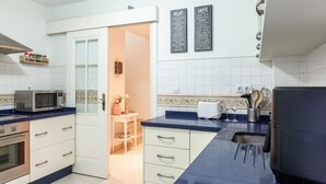 Cozinha moderna com armários brancos, micro-ondas, torradeira e um quadro negro com o cardápio de diversos alimentos.
