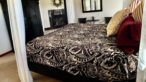 Een slaapkamer met een groot bed, een plafondventilator, een open haard en uitzicht op de omgeving.