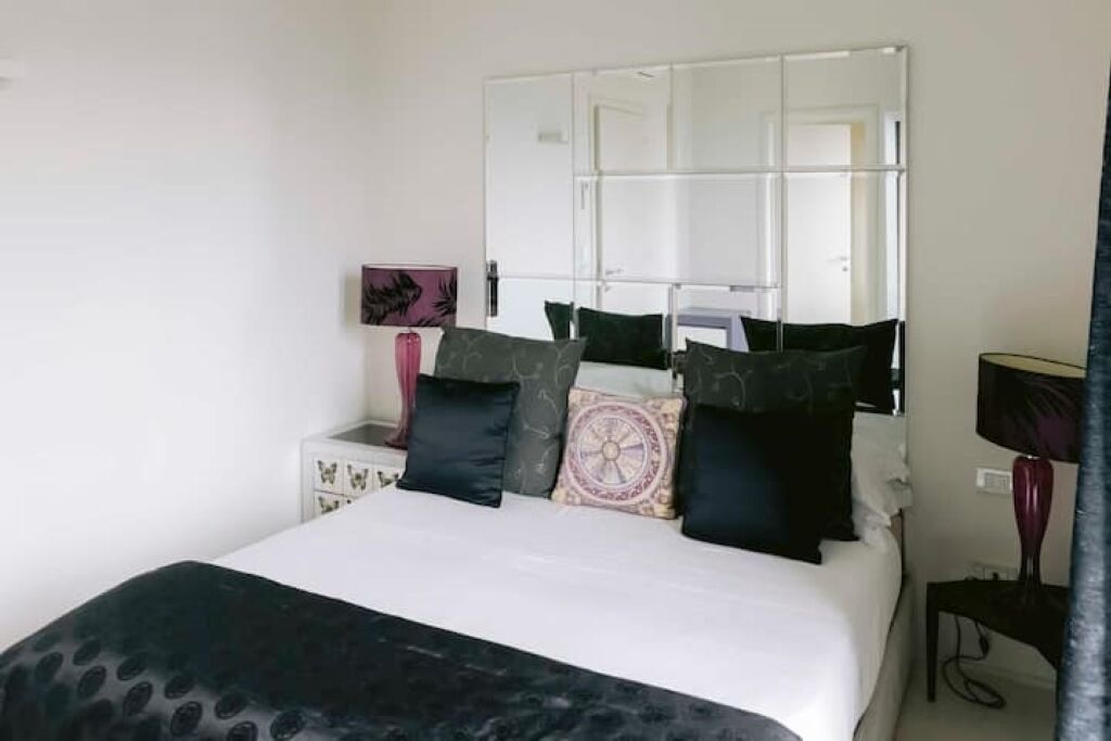 A bedroom with a bed, a bedside table, a mirror, and a lamp.