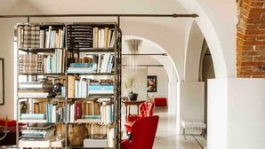 A room with a large bookshelf filled with books, a red chair, and a white bench. - Tenuta Moncarlino - Camera Luce (Piemonte)