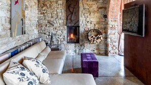 A cozy room with a stone wall, a fireplace, a sofa, and a television. - Tenuta Moncarlino - Camera Luce (Piemonte)