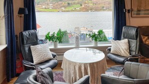 A room with two leather armchairs, a round table, and a view of a lake with boats.