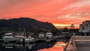 A marina with boats docked, a wooden walkway, and a mountain in the background.