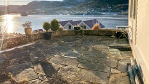 A stone patio with potted plants, a small table, and a view of a river and houses in the distance.