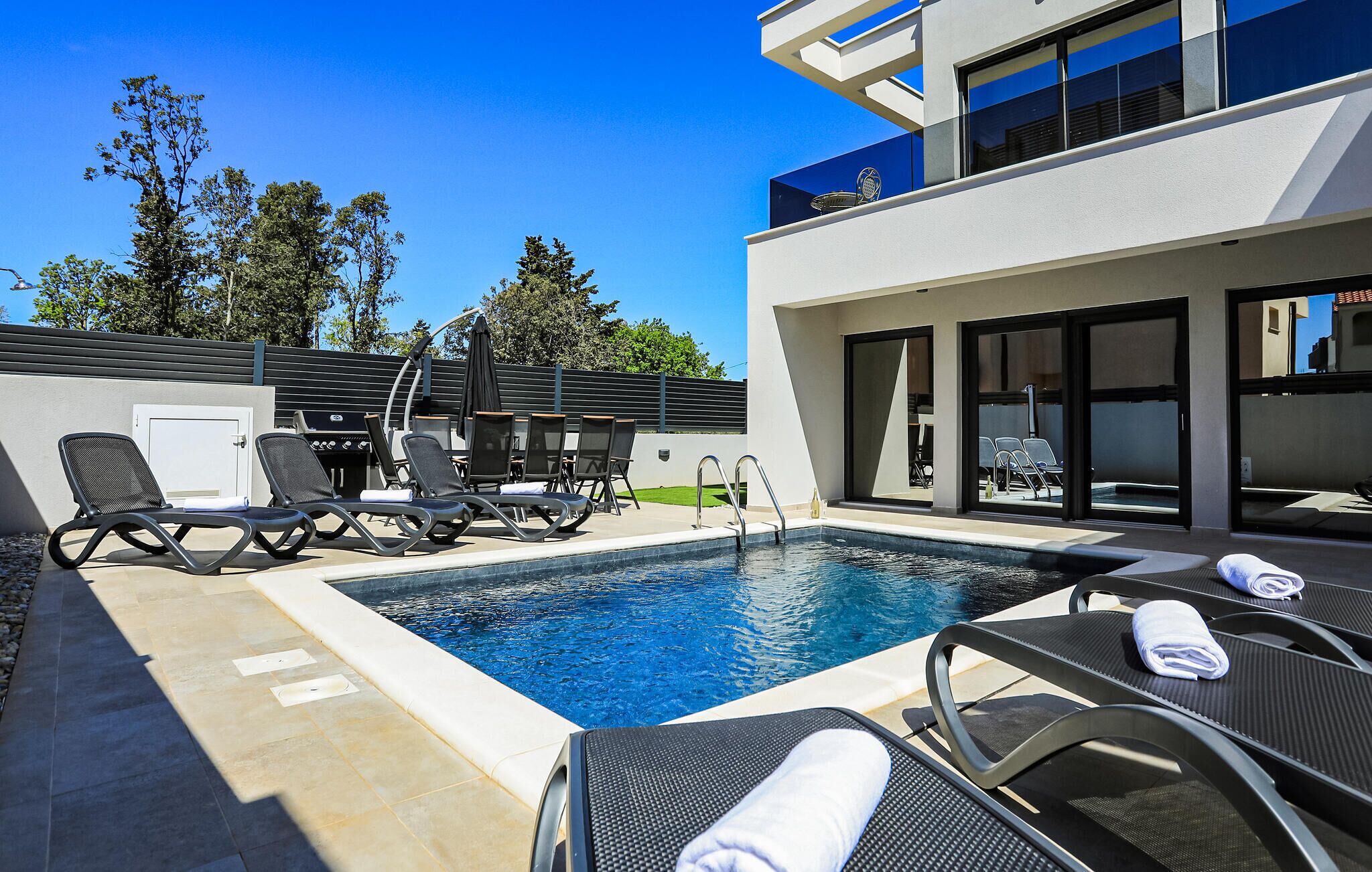A modern outdoor pool area with lounge chairs and a barbecue grill.