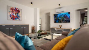 Un soggiorno moderno con un divano, un tavolino in vetro, una televisione e un quadro astratto dai colori vivaci.