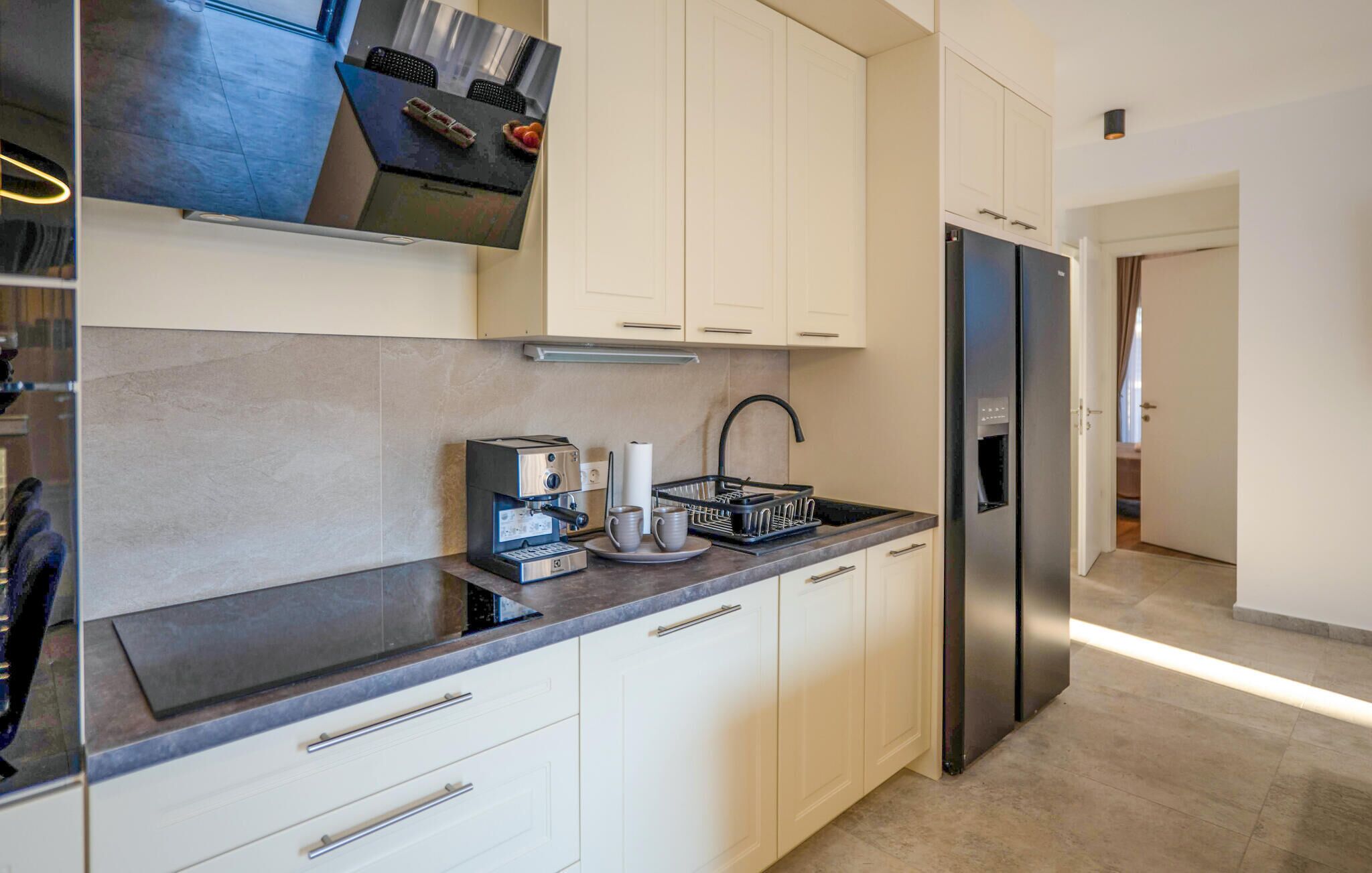 A modern kitchen with a built-in espresso machine, a sink, and a stainless steel refrigerator.