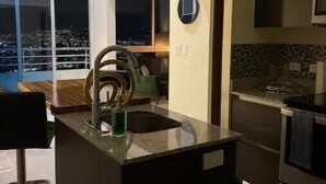 A modern kitchen with a large island, a built-in oven, and a view of the city at night. - Sky View Penthouse Costa Rica (Empalme)