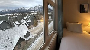Habitación de hotel con un ventanal amplio que ofrece vistas de edificios nevados y montañas.