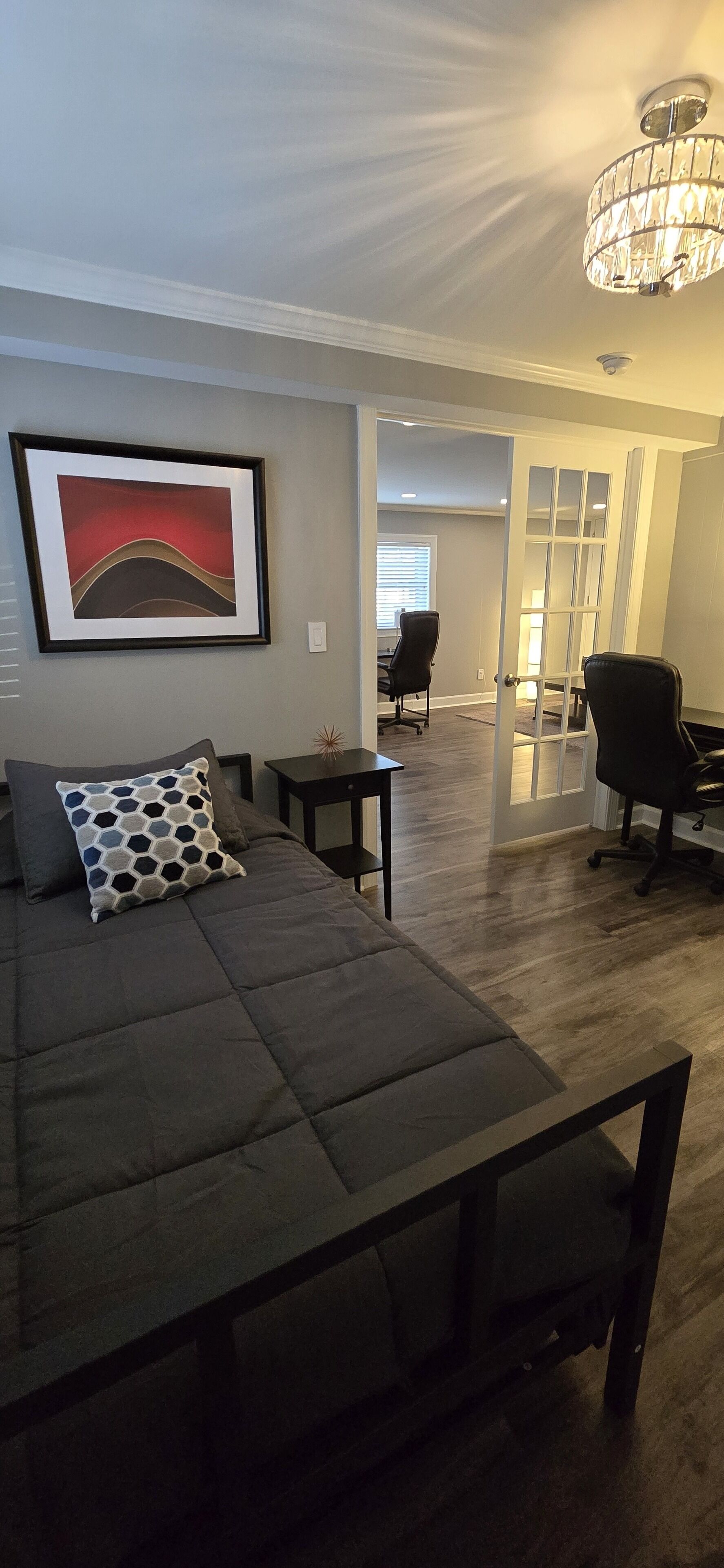 A modern living room with a sectional sofa, a framed abstract painting, and a chandelier.