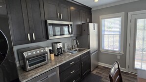 A modern kitchen with dark cabinetry, a built-in microwave, a toaster oven, and a coffee maker. - Deluxe! New Apt Loft Near Downtown – Ready for Families and Business Travelers. (Raleigh)