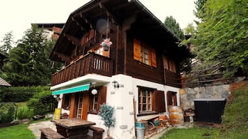 Un chalet en bois doté d’un balcon, de murs en pierre et d’un escalier en pierre menant à l’entrée.