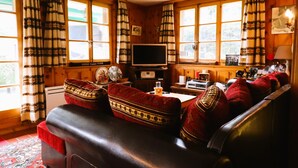 A cozy room with a leather sofa, wooden walls, and large windows with curtains. - Charming detached cottage for up to 5 people. It has a good location close to a shuttle bus stop tha (St-Luc)
