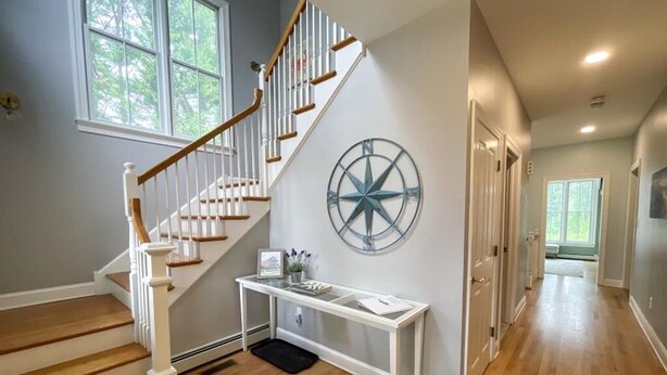 Un escalier avec des marches en bois et des rampes blanches, une décoration en forme de boussole fixée au mur, et une console blanche avec un tapis noir à sa base.
