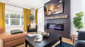 A modern living room with a fireplace, a flat-screen TV, and comfortable seating. - Epic Group Stay: 2 Homes + Hot Tubs + Yard Games (Charlotte)