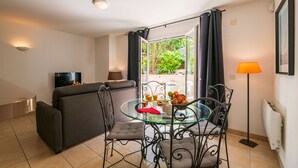 Una sala de estar moderna con un sofá, una mesa de comedor de vidrio con sillas, un televisor y vistas al exterior.