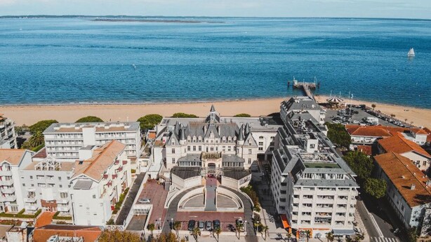 Un paisaje urbano costero con un edificio histórico destacado, una playa y un puerto deportivo.