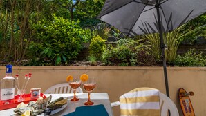 A table set outdoors with a bottle of Abatilles, two glasses of drink, a plate of oysters, and a striped beach chair.
