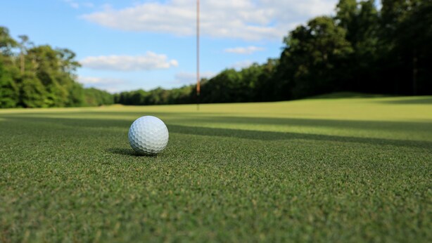 Een golfbal op een verzorgd gazon met een vlag op de achtergrond.