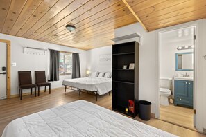 A hotel room with a wooden ceiling, a bed, two chairs, a wardrobe, a bathroom with a toilet and sink, and a window with curtains. - Lift Landing (Idaho Springs)