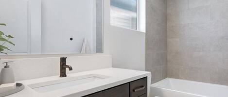 A modern bathroom with a large mirror, dark wood cabinets, a white sink, and a white toilet.